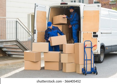 Young Delivery Men Unloading Cardboard Boxes From Truck On Street