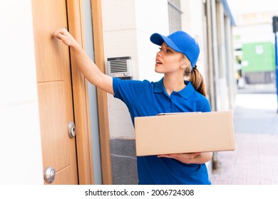 Young Delivery Woman At Outdoors Holding Boxes And Knocking On The Door