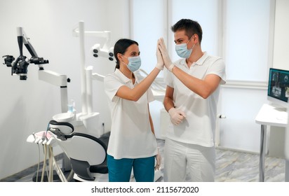 A young dentist and his assistant in a white uniform and medical masks give high five in the dental office. Dentistry and dental care. - Powered by Shutterstock