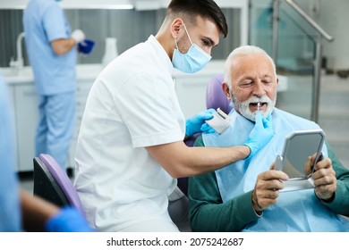 Young dentist and his senior patient choosing right shade of implants during dental appointment. - Powered by Shutterstock