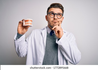 Young dentist man with blue eyes holding orthodontic dental prosthesis over isolated background serious face thinking about question, very confused idea