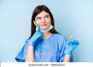 Young dentist woman holding tools over isolated blue background thinking an idea