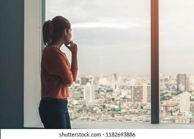 Young depressed asian woman standing alone near window in dark at evening time with low light environment, PTSD Mental health concept, Selective focus.