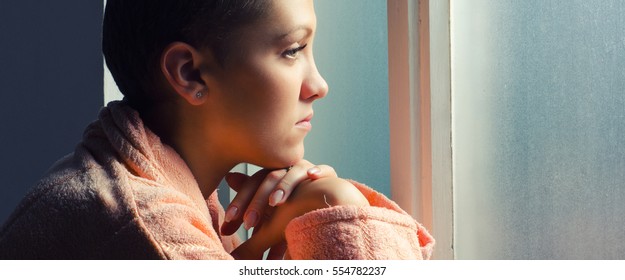 Young depressed cancer patient standing in front of hospital window.