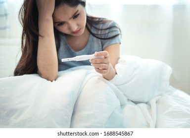 Young depressed and desperate Asian young woman crying and scared testing positive result on pregnancy test alone in bed feeling depressed, remorse and stress in irresponsible mistake concept