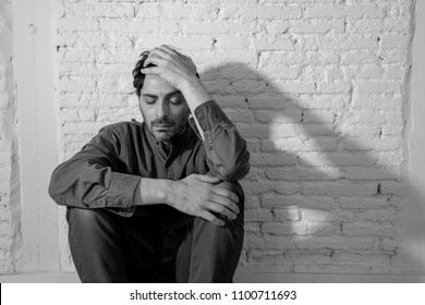 young depressed man sitting against a white wall at home with a shadow on the wall feeling miserable, lonely and sad in mental health depression concept