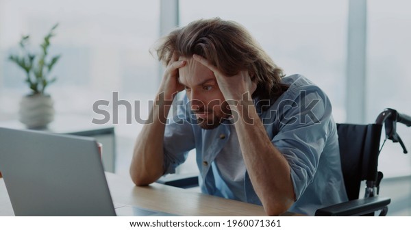 Young depressed office worker sitting by desk worry\
about work. Disabled invalid young man frutrating having problems\
at work.