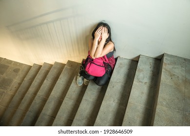 young depressed and scared Asian Japanese student girl suffering abuse and harassment at school victim of bullying and discrimination sitting on college staircase tormented - Powered by Shutterstock