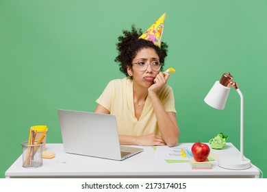 Young Depressed Upset Sad Employee Business Woman Of African American Ethnicity Wear Shirt Birthday Hat Sit Work At White Office Desk With Pc Laptop Prop Up Chin Isolated On Plain Green Background.