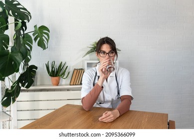 Young Depressed Woman Doctor Sitting In The Room At The Hospital Taking A Break From Stressed Work. Female Medical Worker Under The Psychical Pressure Resting Alone From Hard Work At The Clinic.