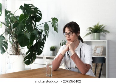 Young Depressed Woman Doctor Sitting In The Room At The Hospital Taking A Break From Stressed Work. Female Medical Worker Under The Psychical Pressure Resting Alone From Hard Work At The Clinic.