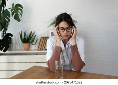 Young Depressed Woman Doctor Sitting In The Room At The Hospital Taking A Break From Stressed Work. Female Medical Worker Under The Psychical Pressure Resting Alone From Hard Work At The Clinic.