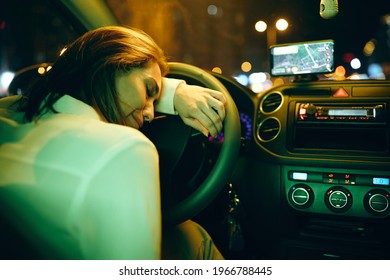 Young Depressed Woman Leaning On Steering Wheel And Crying While Driving Car At Night. 