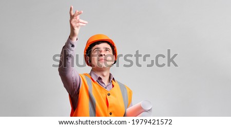 young design engineer in hard hat and reflective vest on grey studio background showing with handup, foreman managing