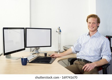 Young Design Engineer, Using A Powerful Computer Aided Design (CAD) Workstation Sitting Confidently Behind His Desk, Smiling