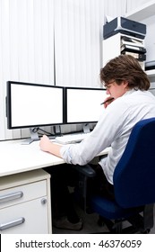 A Young Designer Chewing His Pen In Thoughts, Sitting Behind A Computer Work Station.