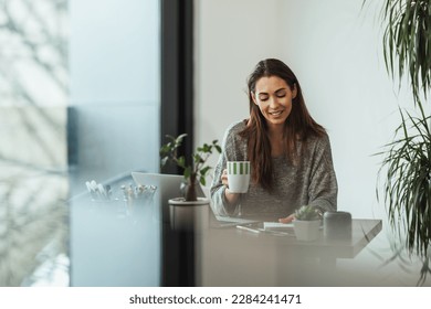 Young designer drinking coffee while working from her home studio.