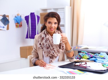 Young designer woman sitting on the desk with cup