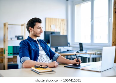 Young designer working with graphics tablet and laptop at desk in small office