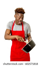 Young Desperate And Confused Black Afro American Man In Chef Apron Holding Cooking Pot And Spoon In His Hands Looking Lost And Overworked In Male Home Cook Concept Isolated On White Background