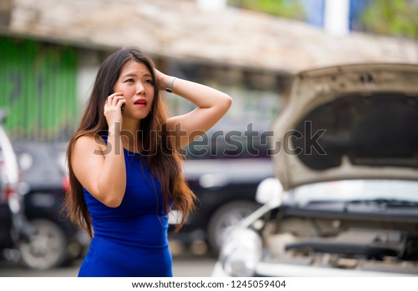 young desperate and upset Asian Chinese woman in stress
stranded on street suffering car engine failure having mechanic
problem calling on mobile phone for help to insurance assistance
service 