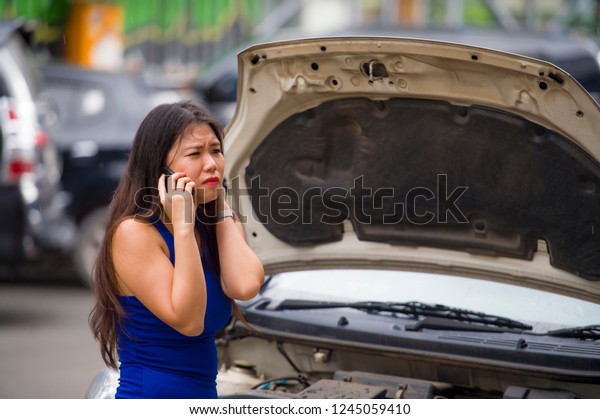 young desperate and upset Asian Chinese woman in stress\
stranded on street suffering car engine failure having mechanic\
problem calling on mobile phone for help to insurance assistance\
service 