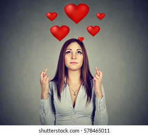 Young desperate woman in love making a wish keeps her fingers crossed isolated on gray background