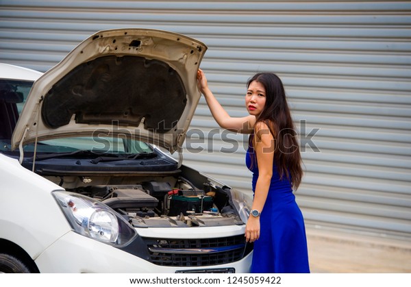 young\
desperate and worried Asian Japanese woman in stress stranded on\
street roadside with car engine failure having mechanic problem\
needing repair service feeling helpless and\
annoyed