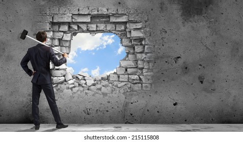 Young determined businessman breaking wall with hammer - Shutterstock ID 215115808
