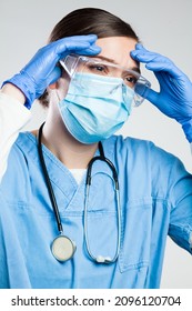 Young Devastated Female NHS General Practitioner Doctor Wearing Face Mask And Protective Eyewear,head In Hands,death Of Many Patients Due To Increased Spread Of Coronavirus,COVID-19 Pandemic Crisis