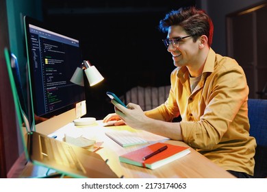 Young Developer Geek Software Engineer IT Specialist Programmer Man In Shirt Work At Home Writing Code On Laptop Pc Computer, Using Mobile Cell Phone Application, Browsing. Program Development Concept