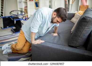 Young Disable Man In Casualwear Trying To Get Up On Sofa From The Floor After Falling Off Wheelchair