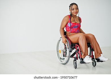 Young disabled African American woman in wheelchair against white wall.
