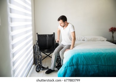 Young disabled man using all his strength to move from his bed to a wheelchair by himself at home - Powered by Shutterstock