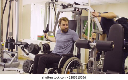 Young disabled man in wheelchair doing strength exercises for hands in the rehabilitation clinic. Doctor physiotherapist helping him
