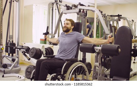 Young disabled man in wheelchair doing strength exercises for hands in the rehabilitation clinic. Doctor physiotherapist helping him