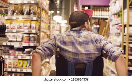 Young disabled man in a wheelchair riding in the supermarket. Rear view