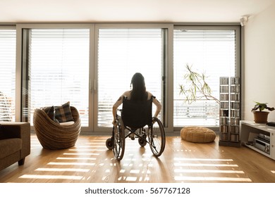 Young Disabled Woman In Wheelchair At Home, Rear View.