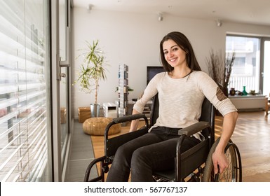Young disabled woman in wheelchair at home in living room.