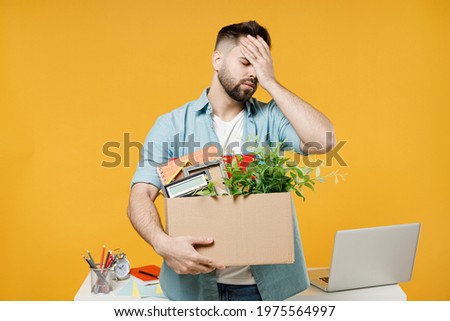 Young disappointed employee business man in shirt stand work white office desk pc laptop hold cardboard box with stuff put hand on face facepalm epic fail gesture isolated on yellow background studio