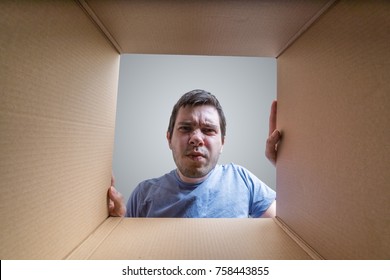 Young Disappointed Man Is Looking On Gift Inside Cardboard Box.