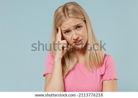 Young disappointed worried sad caucasian blonde woman 20s in casual pink t-shirt prop up forehead look camera isolated on plain pastel light blue background studio portrait. People lifestyle concept