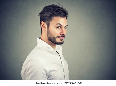 Young dishonest man in white shirt looking with pretend smile at camera on gray background