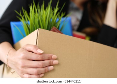 Young dismissed female worker in office holding carton box with her belongings. Getting fired concept.