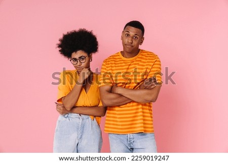 Young displeased african man and woman standing with irritated look isolated over pink studio wall