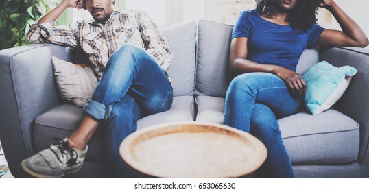 Young Displeased Black Couple.American African Men Arguing With His Stylish Girlfriend,who Is Sitting On Sofa On Couch Next To Him With Legs Crossed.Man Looking Away Offended.Horizontal,cropped