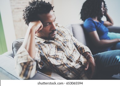 Young Displeased Black Couple.Upset Man Being Ignored By Partner At Home In The Living Room.American African Men Arguing With His Stylish Girlfriend,who Is Sitting On Sofa Couch Next To Him.Blurred.