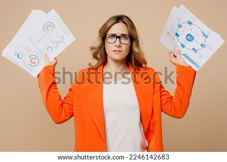 Young displeased sad dissatisfied employee business woman corporate lawyer 30s wears classic formal orange suit glasses work in office hold paper docements isolated on plain beige background studio