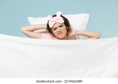 Young Displeased Tired Woman In Pajamas Jam Sleep Eye Mask Rest Relax At Home Lie In Bed Pillow Under Blanket Hold Hand Behind Neck Isolated On Pastel Blue Background Bad Mood Night Bedtime Concept.