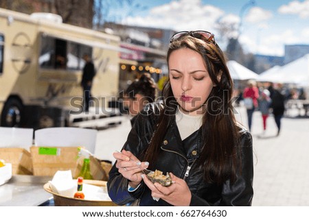 Young displeased woman holding a single fresh opened oyster at outdoor food festival